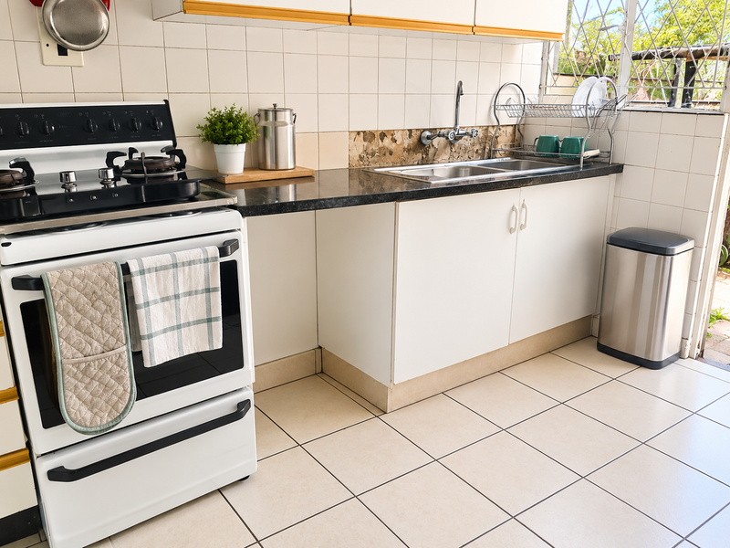 A functional kitchen featuring a gas stove, double sink, tiled backsplash, and white cabinetry with dark countertops, offering a practical layout for daily use.