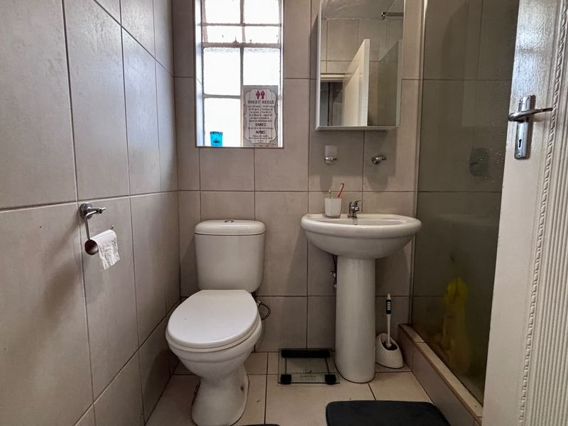 A functional bathroom featuring a pedestal washbasin, toilet, and a glass-enclosed shower, finished with neutral wall and floor tiles.
