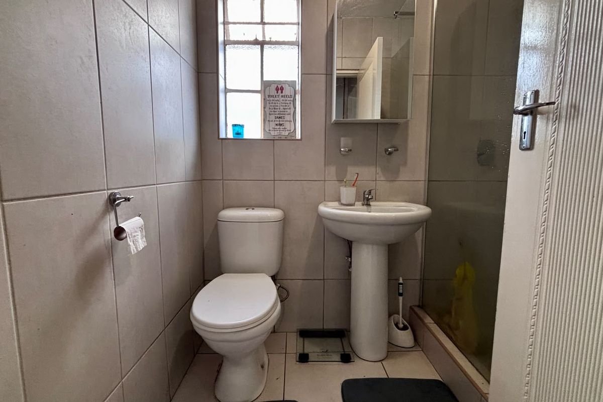 A functional bathroom featuring a pedestal washbasin, toilet, and a glass-enclosed shower, finished with neutral wall and floor tiles.
