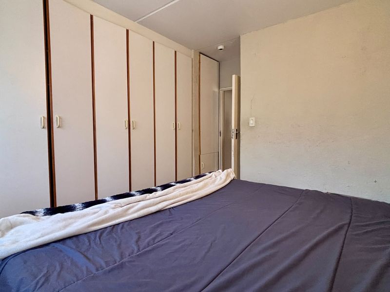 A bedroom featuring extensive built-in cupboards and a standard door, requiring minor cosmetic updates to the wall finishes.