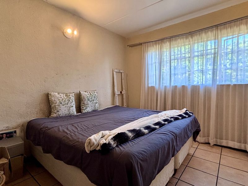 A bedroom featuring tiled flooring, a built-in cupboard, and a large window with curtain rails, requiring cosmetic updates to the wall finishes.