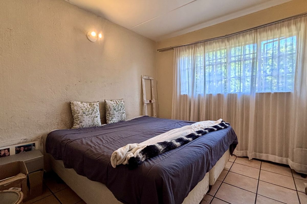 A bedroom featuring tiled flooring, a built-in cupboard, and a large window with curtain rails, requiring cosmetic updates to the wall finishes.