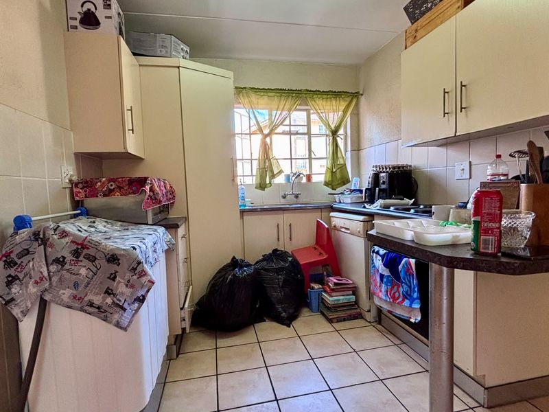 A compact kitchen featuring built-in cabinetry, tiled flooring, and a functional layout with a stainless steel sink and integrated cooking appliances.