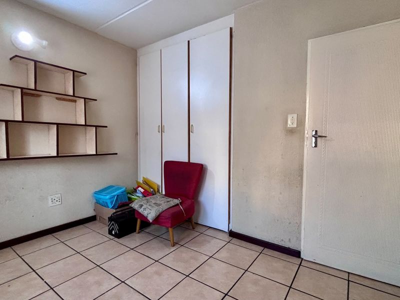 A bedroom featuring tiled flooring, built-in cupboards, and wall-mounted shelving, requiring cosmetic updates to the wall finishes.