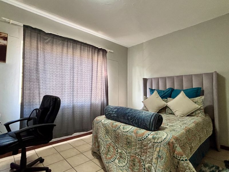 A functional bedroom featuring tiled flooring and a window with curtain rod, offering a neutral space ready for personalization.