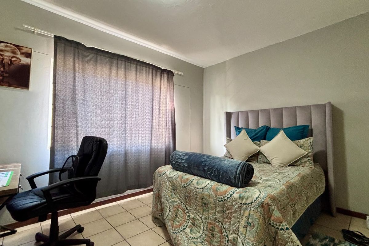 A functional bedroom featuring tiled flooring and a window with curtain rod, offering a neutral space ready for personalization.