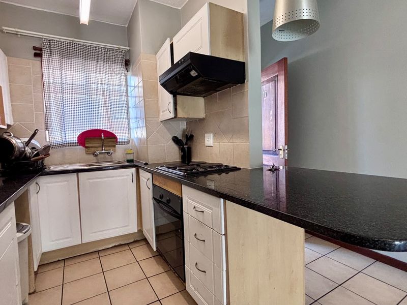 A functional kitchen featuring granite countertops, built-in cabinetry, a gas hob, and an integrated oven with a breakfast bar extension.
