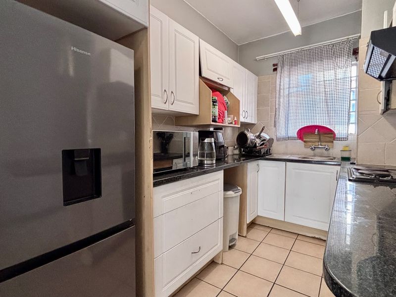 A functional kitchen featuring white cabinetry, dark granite countertops, tiled flooring, and a built-in extractor fan.