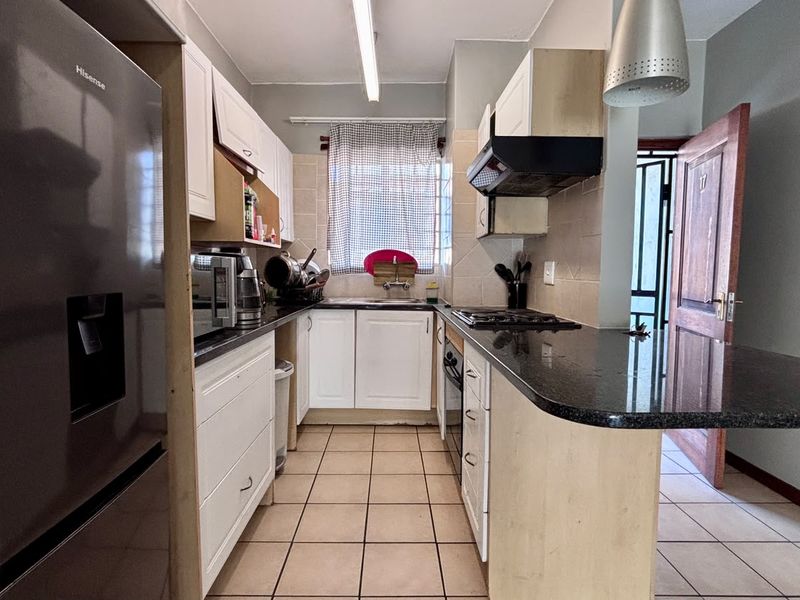 Functional kitchen featuring white cabinetry, granite countertops, built-in oven, gas hob, and a breakfast bar, with tiled flooring throughout.