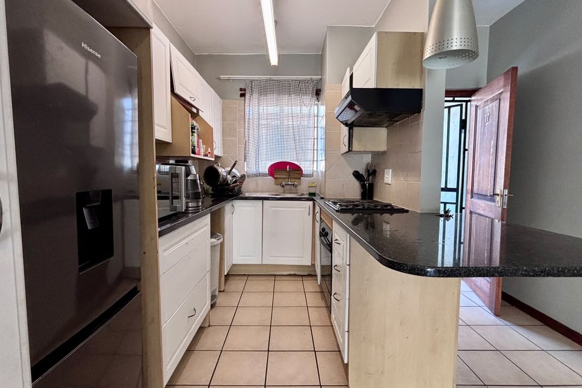 Functional kitchen featuring white cabinetry, granite countertops, built-in oven, gas hob, and a breakfast bar, with tiled flooring throughout.
