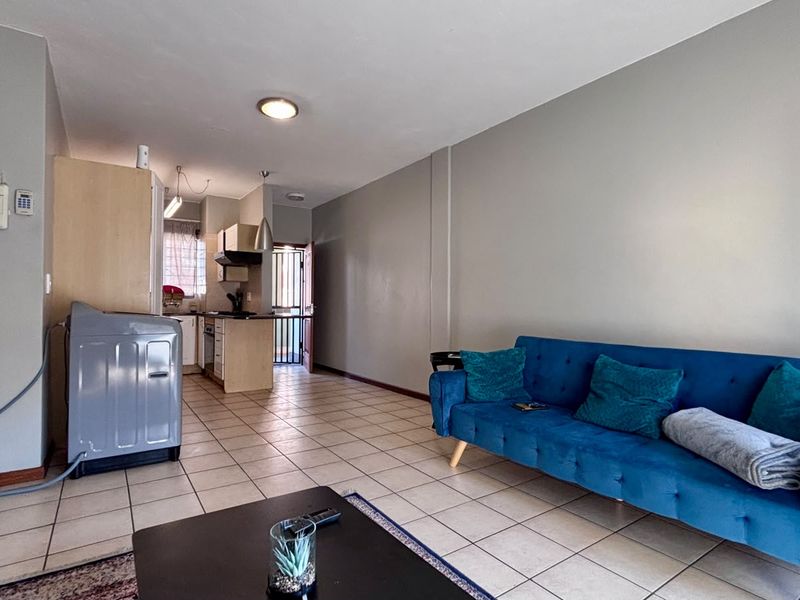Open-plan living area featuring tiled flooring and a compact kitchen with built-in cabinetry, leading to an exterior entrance.