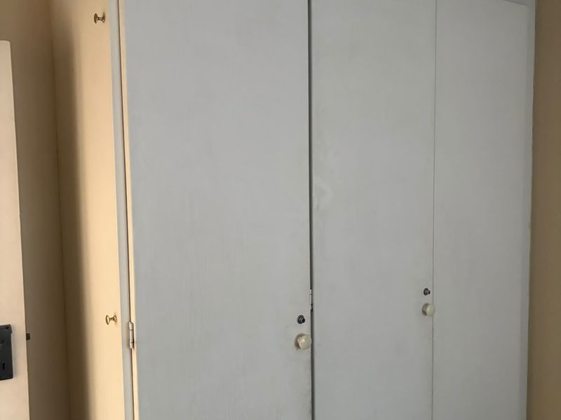 A bedroom featuring a built-in wardrobe with white painted doors, showing signs of wear and age.