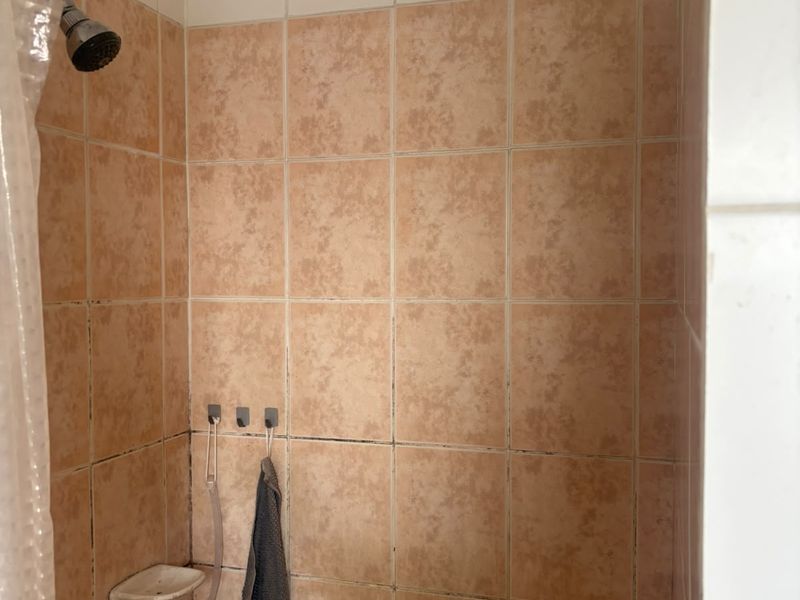 A shower enclosure featuring dated peach-toned ceramic wall tiles and a standard shower head, requiring cosmetic updates to grout and finishes.