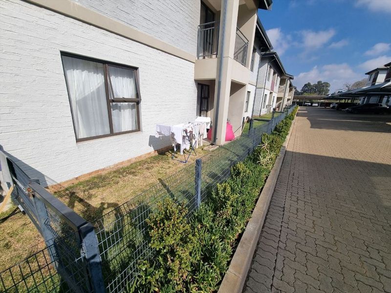 Exterior view of the apartment building featuring a brick facade, small private garden area, metal fencing, and paved driveway access.