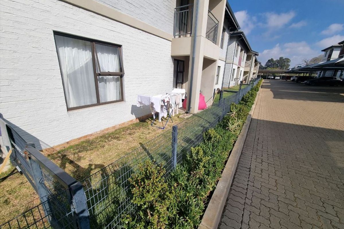 Exterior view of the apartment building featuring a brick facade, small private garden area, metal fencing, and paved driveway access.