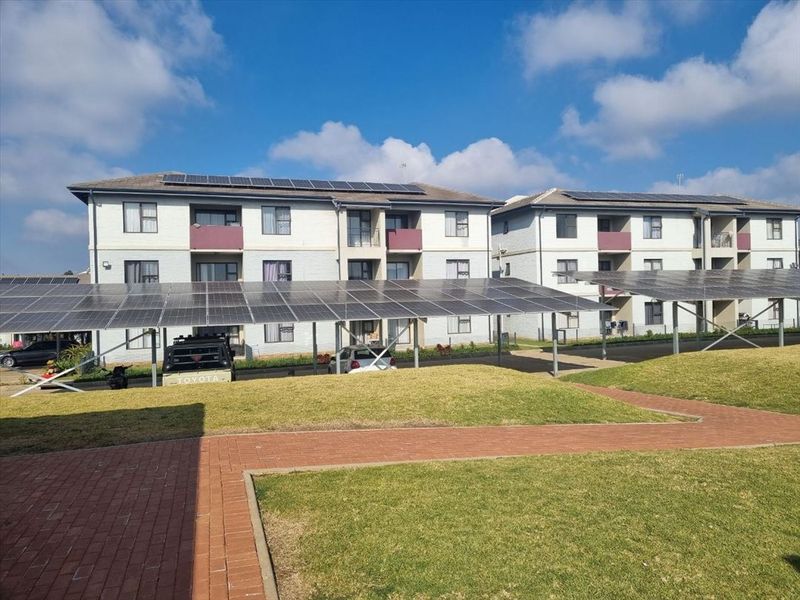 Exterior view of an apartment complex featuring a well-maintained lawn, paved walkways, and extensive solar panel installations over the parking area.