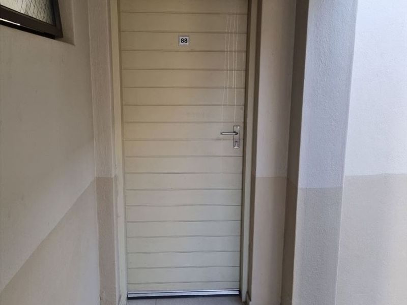 A clean and functional apartment entrance featuring a horizontal panel door, tiled flooring, and a high-level window for natural light.