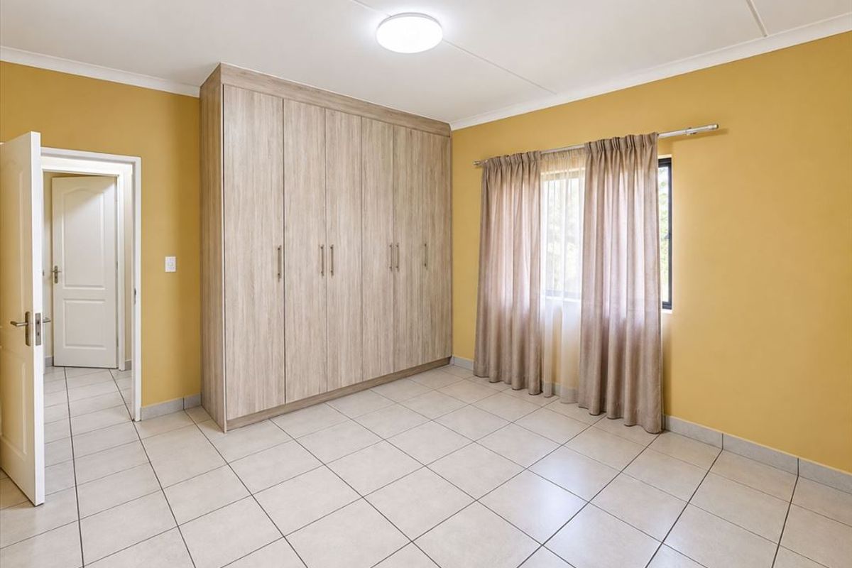 A clean, empty bedroom featuring neutral tiled flooring, built-in wooden cupboards, and a bright, functional layout ready for personalization.