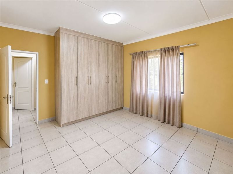 A clean, empty bedroom featuring neutral tiled flooring, built-in wooden cupboards, and a bright, functional layout ready for personalization.