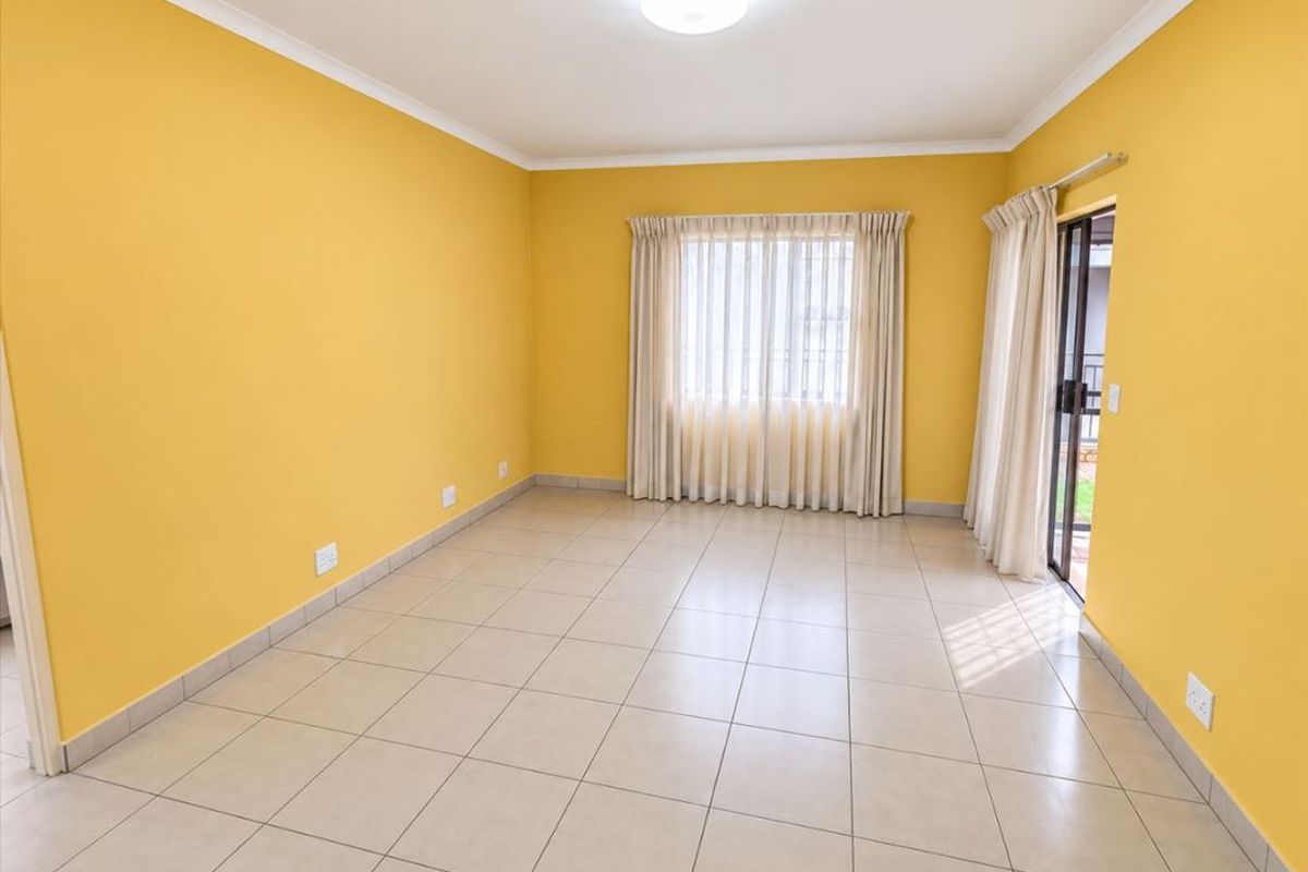 A bright, empty living room featuring tiled flooring, yellow walls, and a sliding glass door providing access to the exterior.