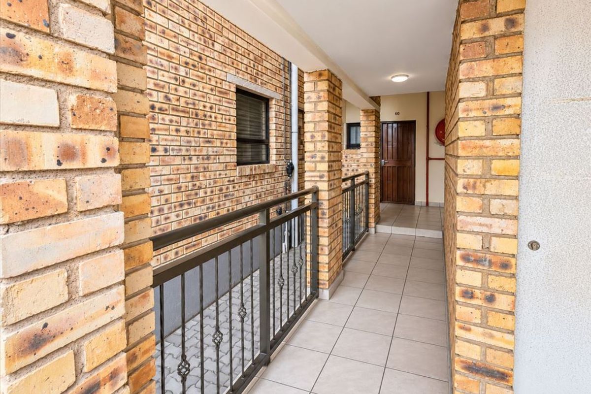 A clean, well-maintained apartment hallway featuring face brick walls, tiled flooring, and a secure metal balustrade.