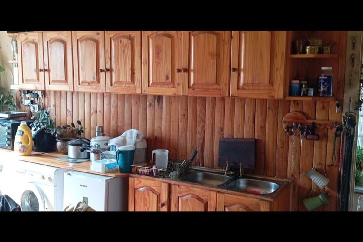 A dated kitchen area featuring extensive wooden cabinetry and wall paneling with a double stainless steel sink and integrated appliance space.