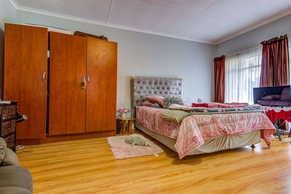 A spacious bedroom featuring light-toned laminate flooring and large windows with curtain rails, offering a neutral base for personalization.