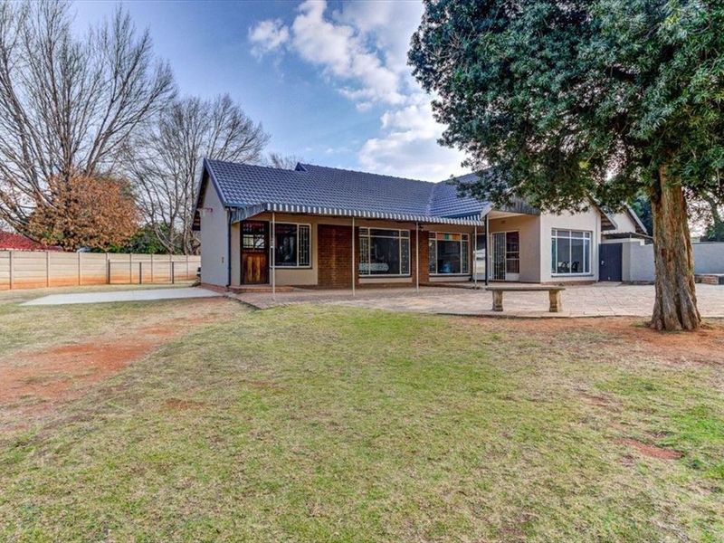 Rear view of the house featuring a paved patio area, tiled roof, and a spacious garden with perimeter walling.