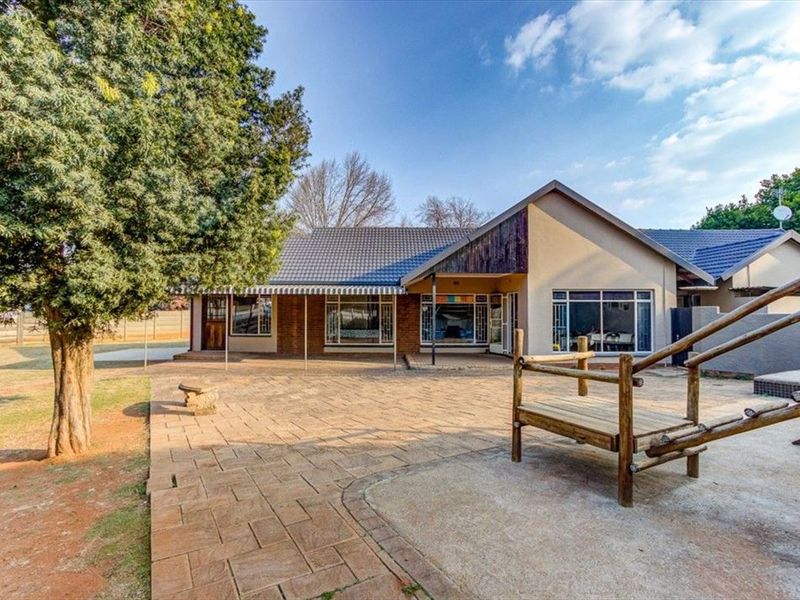 Spacious rear exterior view featuring a large paved patio area, brick and rendered facade, and extensive glazing overlooking the garden.