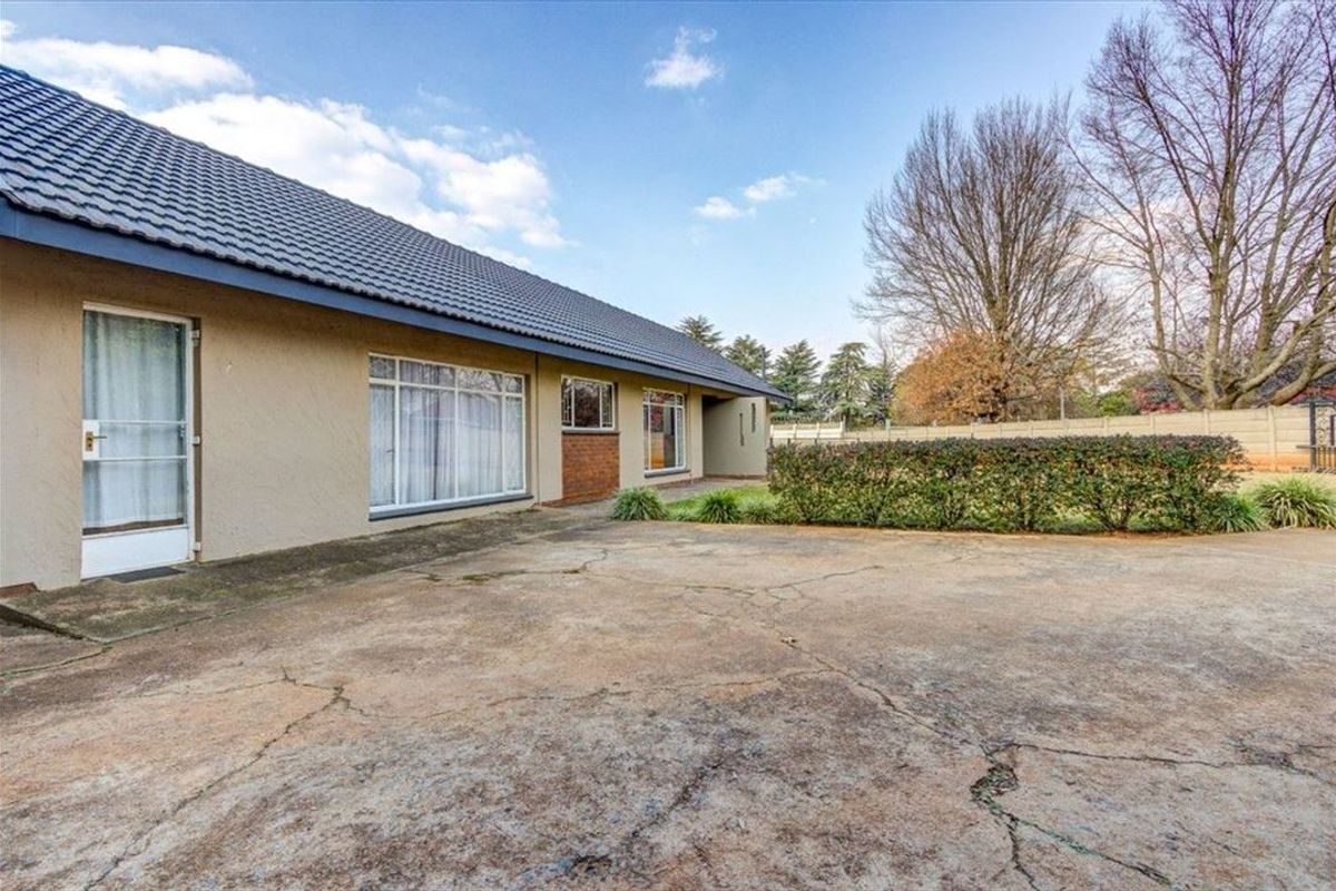 Rear exterior view of the house featuring a large concrete driveway, plastered walls, tiled roof, and a garden area with boundary walling.