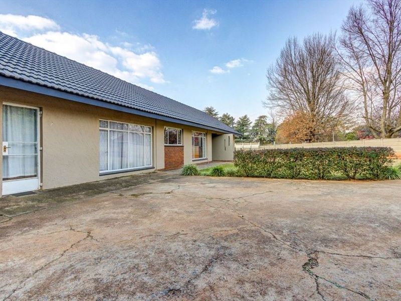 Rear exterior view of the house featuring a large concrete driveway, plastered walls, tiled roof, and a garden area with boundary walling.