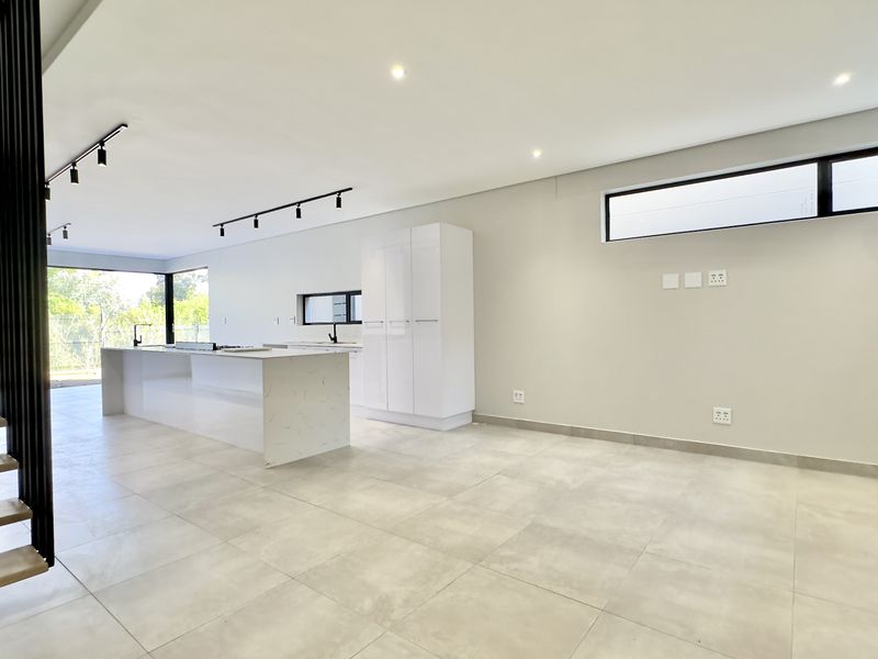 Spacious open-plan living and kitchen area featuring a modern island, sleek cabinetry, and a contemporary staircase in a bright, neutral setting.