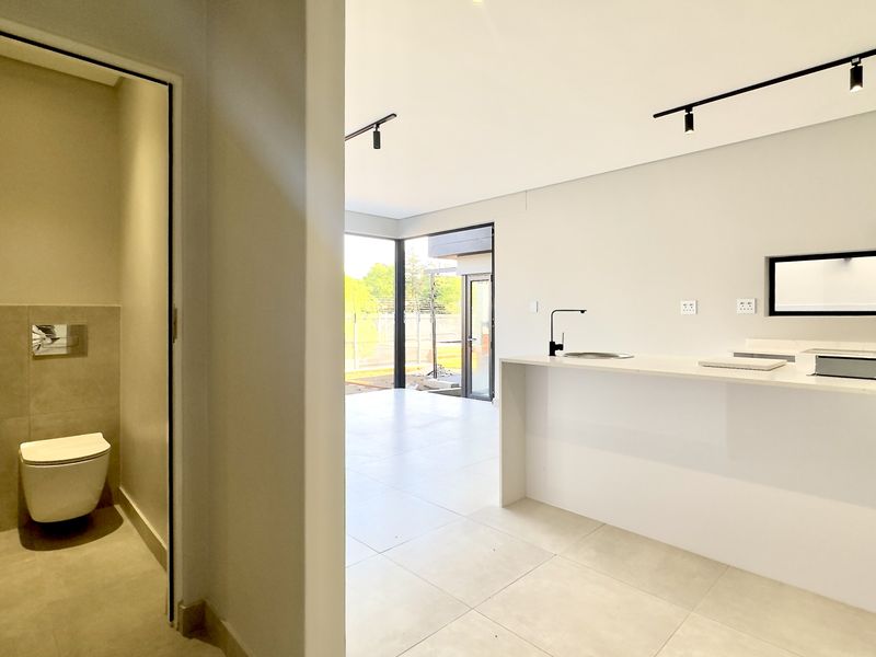 Modern open-plan living area featuring a sleek kitchen with stone countertops and an adjacent guest bathroom with contemporary fixtures and neutral tiling.