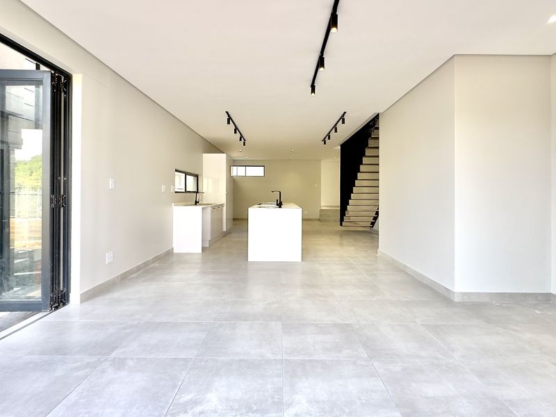 Spacious open-plan living and kitchen area featuring modern tiled floors, a central kitchen island, sleek track lighting, and large bi-fold doors leading outdoors.