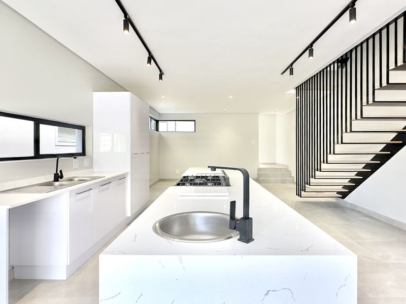 Modern open-plan kitchen featuring a large island with quartz countertops, gas hob, sleek white cabinetry, and a striking floating staircase with metal balustrade.