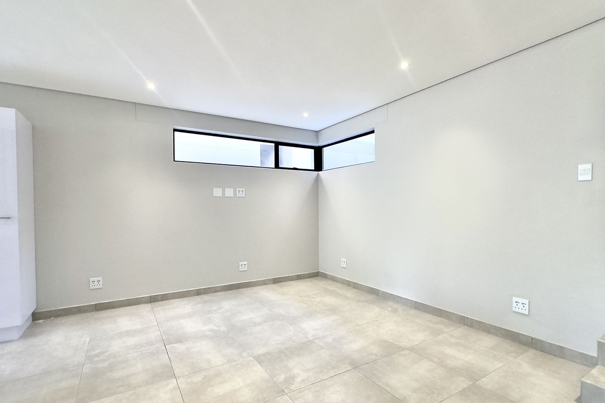 A bright, modern, and empty living area featuring neutral tiled flooring, recessed downlights, and corner clerestory windows providing natural light.