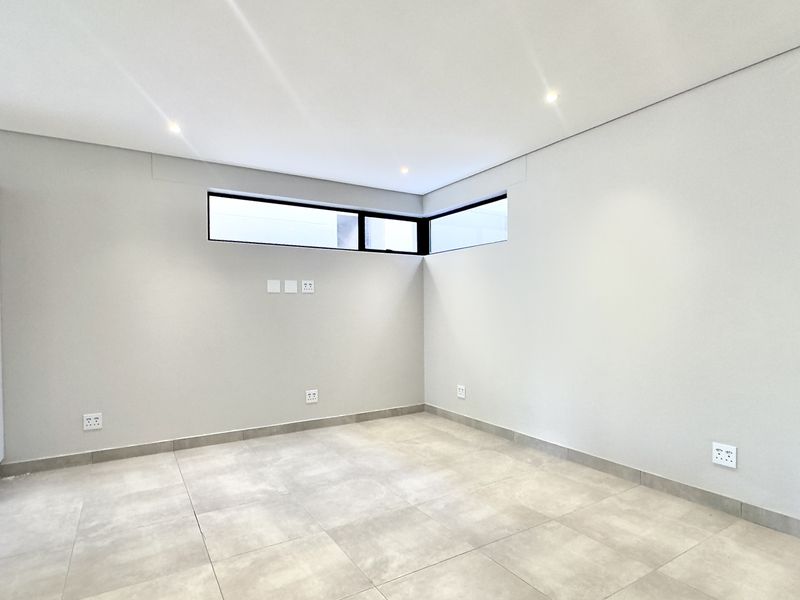 A bright, modern, and empty living area featuring neutral tiled flooring, recessed downlights, and corner clerestory windows providing natural light.