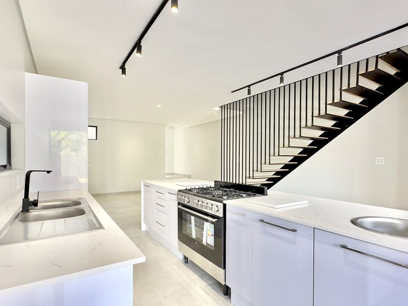 Modern open-plan kitchen featuring sleek white cabinetry, quartz countertops, gas stove, and a striking staircase with a contemporary metal balustrade.