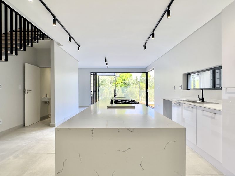 Modern open-plan kitchen featuring a large stone island, sleek cabinetry, track lighting, and seamless access to the outdoor area via bi-fold doors.