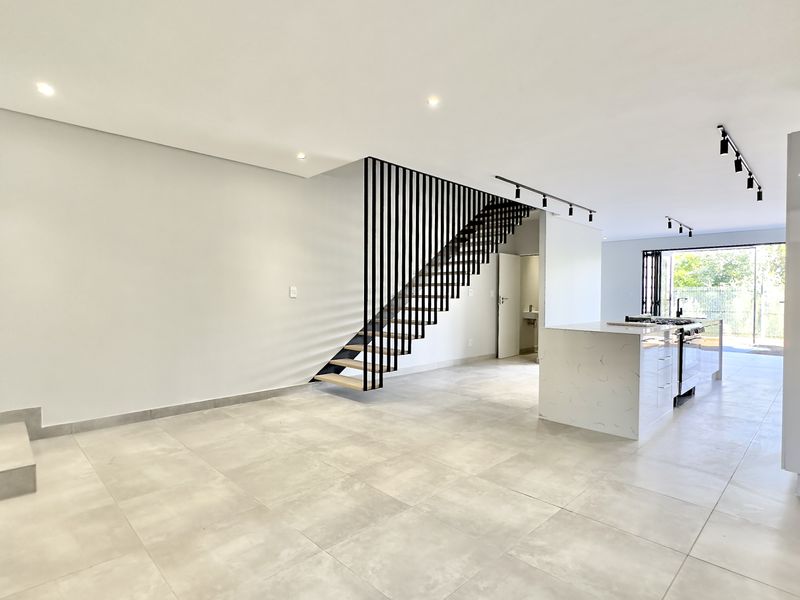 Spacious open-plan living and kitchen area featuring modern tiled floors, a striking staircase with metal balustrades, and seamless access to the outdoor space.