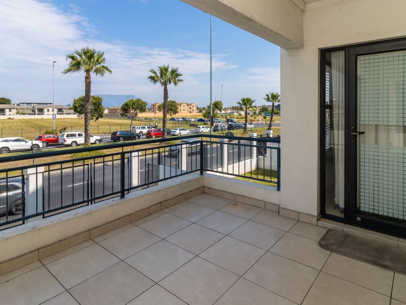 A spacious covered balcony featuring tiled flooring and a metal balustrade, offering an open view of the surrounding neighborhood and street.