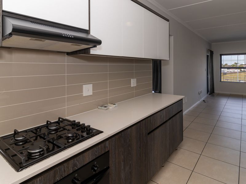 Modern open-plan kitchen featuring sleek cabinetry, stone countertops, gas hob, and extractor fan, flowing into a spacious living area with tiled flooring.