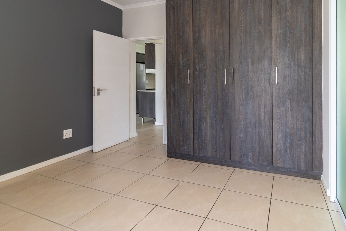 A clean, empty bedroom featuring modern dark wood built-in cupboards, neutral tiled flooring, and a contemporary grey accent wall.
