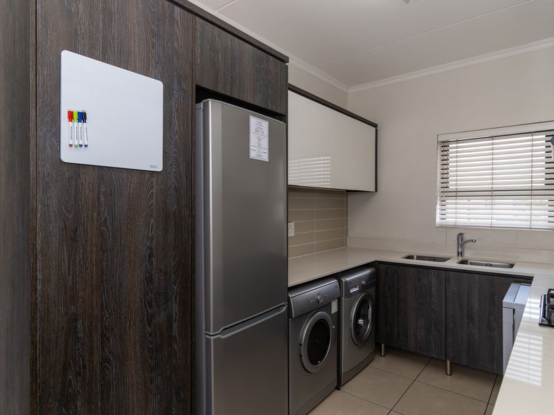 Modern kitchen featuring dark wood-grain cabinetry, stone countertops, a gas hob with extractor, and integrated space for laundry appliances.