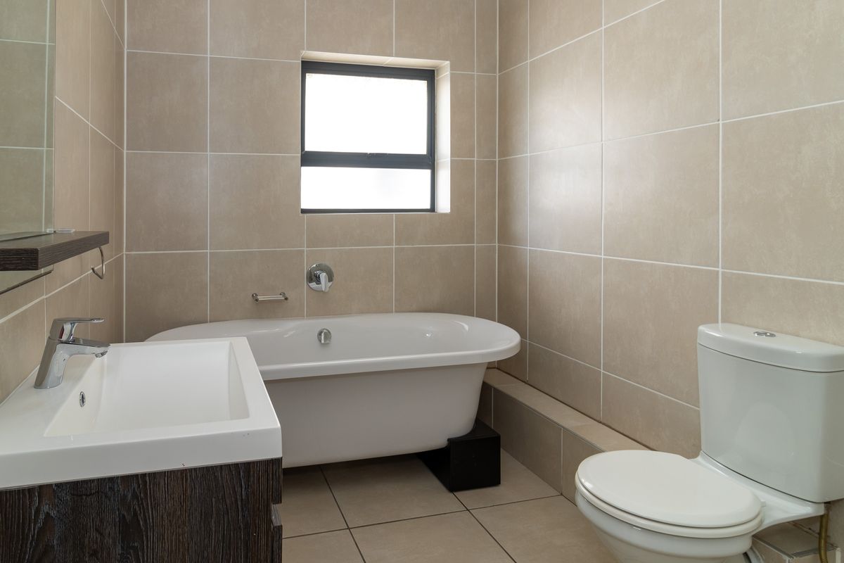 A clean, modern bathroom featuring a freestanding bathtub, vanity cabinet with basin, and neutral wall and floor tiling.