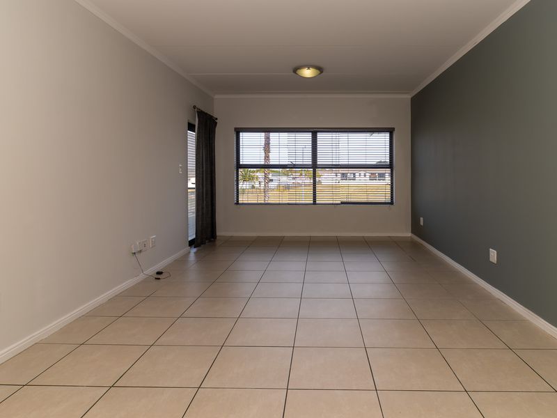A spacious, empty living room featuring neutral tiled flooring, a dark grey accent wall, and large windows with fitted blinds.
