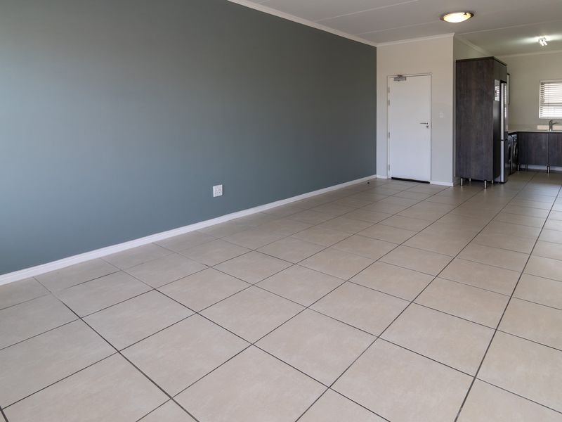 Spacious open-plan living area featuring neutral tiled flooring, a modern grey accent wall, and an integrated kitchen with built-in cabinetry and appliances.