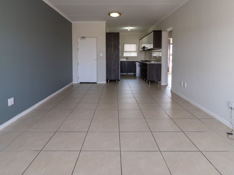 Spacious open-plan living area featuring neutral tiled flooring, a modern kitchen with built-in cabinetry, and a contemporary grey accent wall.