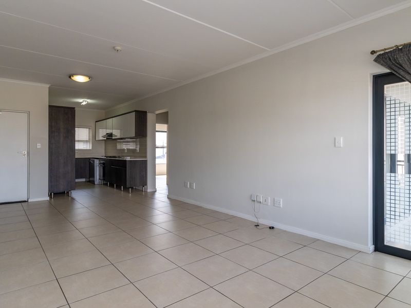 Spacious open-plan living area featuring neutral tiled flooring, a modern kitchen with built-in cabinetry, and direct access to a balcony through a sliding door.