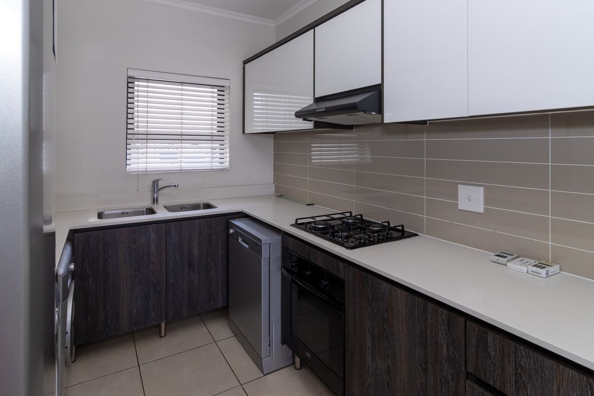 Modern kitchen featuring dark wood-grain lower cabinetry, white upper cabinets, stone countertops, gas hob, built-in oven, and a double sink with tiled backsplash.